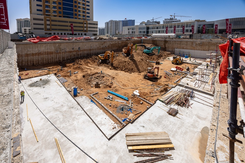 Cove Edition I By Imtiaz 1 Construction site with heavy machinery, excavated ground, and workers amidst buildings under development.